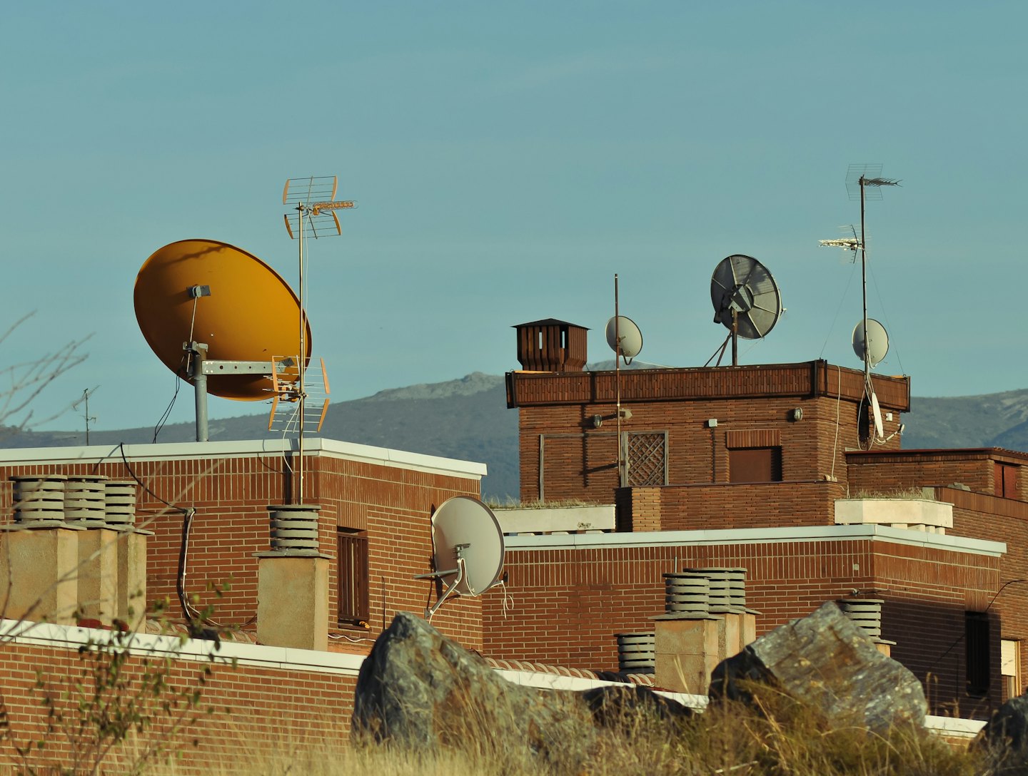 Satellite dishes and antennas on red brick building rooftops.