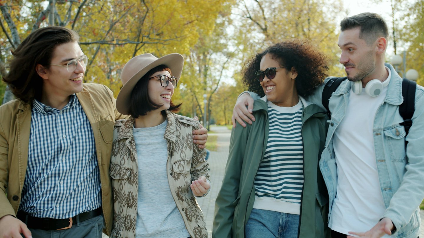 Four friends walk arm-in-arm along an autumn park path.
