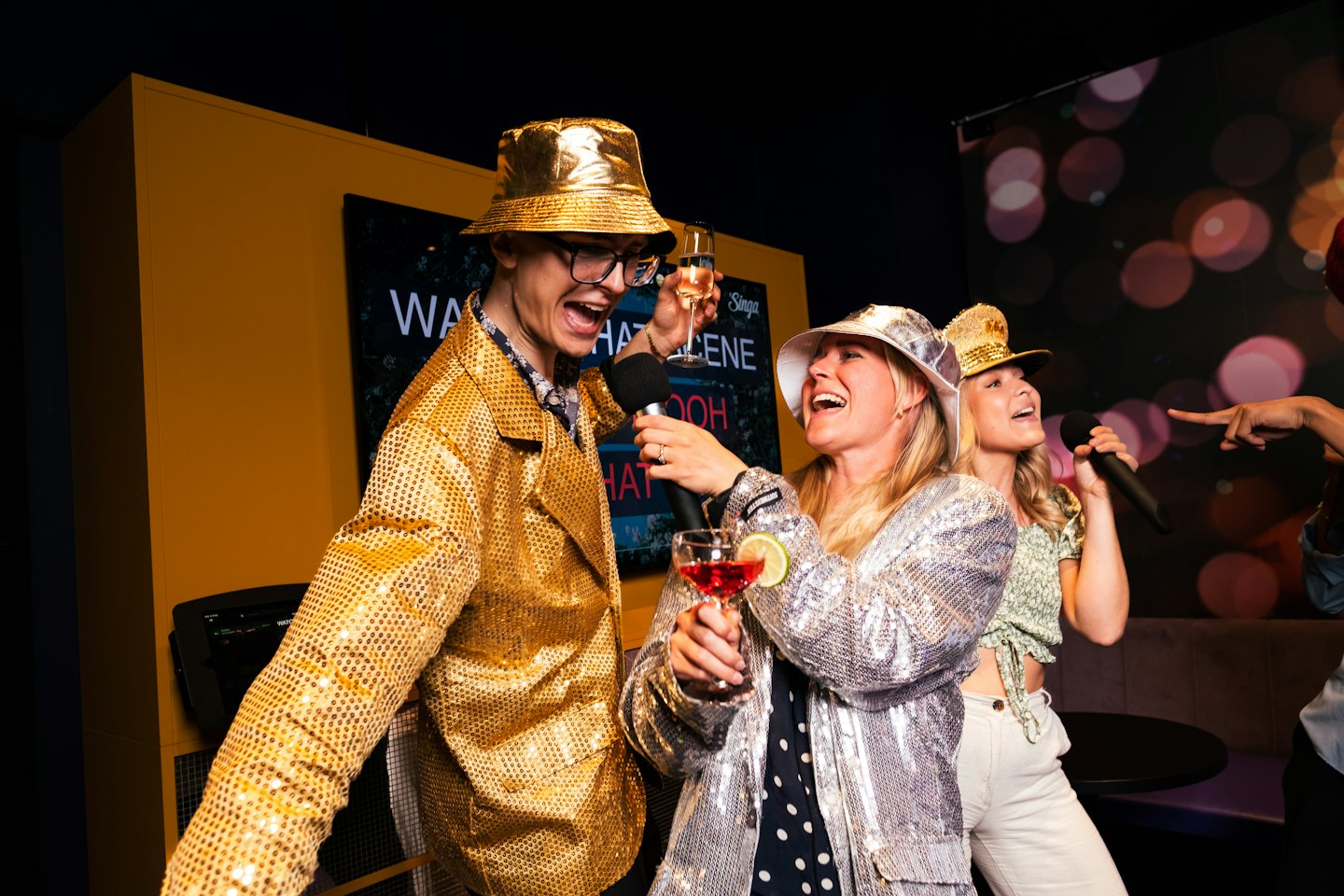 Friends singing karaoke while wearing festive outfits and holding drinks.